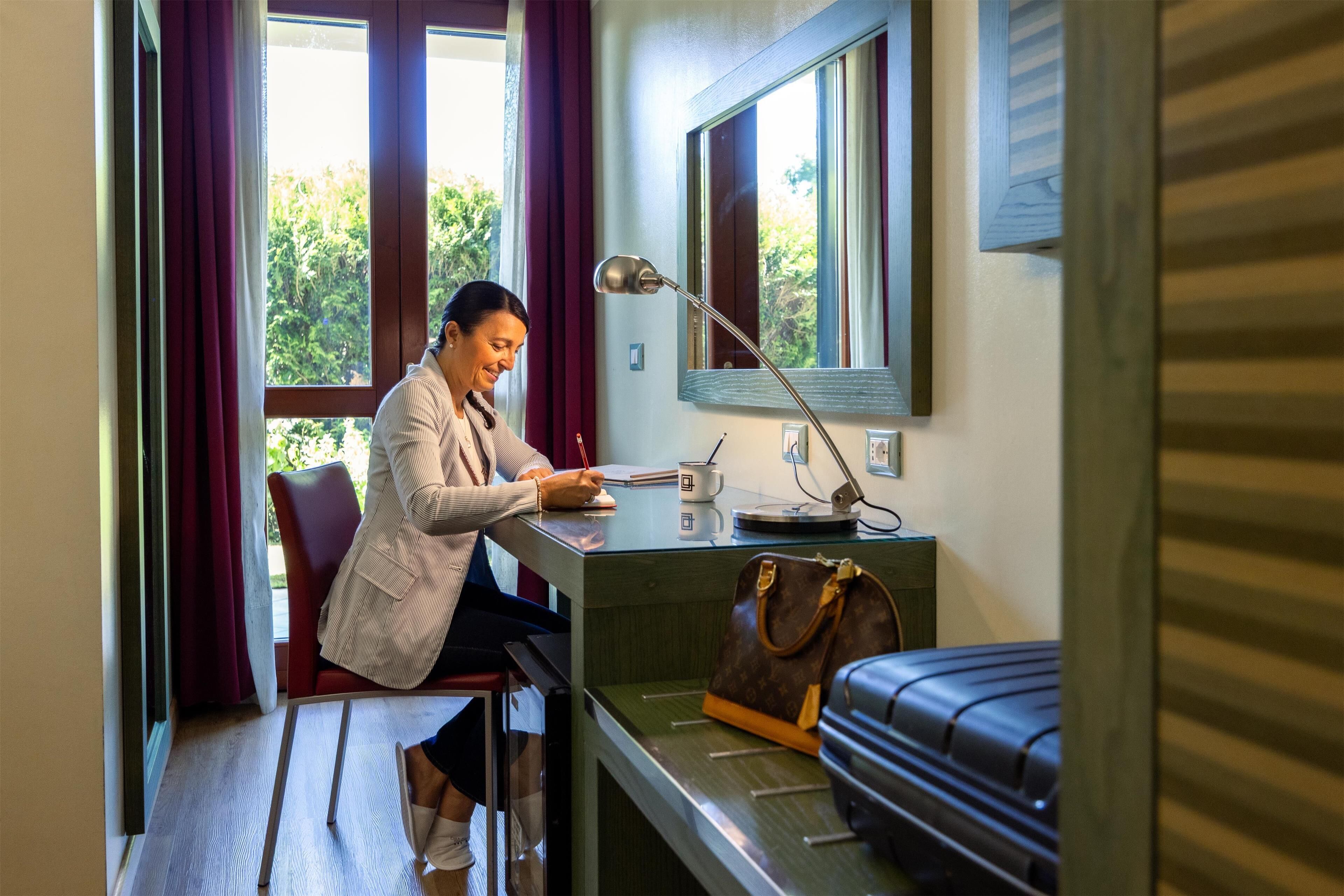 Une pièce comprenant un bureau, une chaise, une fenêtre avec des rideaux, une lampe, une valise et un sac à main.