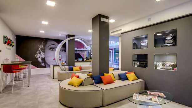A modern interior with a curved sofa, a glass coffee table, and a bar area with stools and a mirror. - La Villa, Sure Hotel Collection by Best Western (Ivrea)