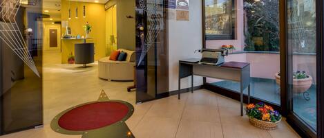 A hotel reception area with a desk, a computer, a telephone, and a seating area with a sofa and a chair.