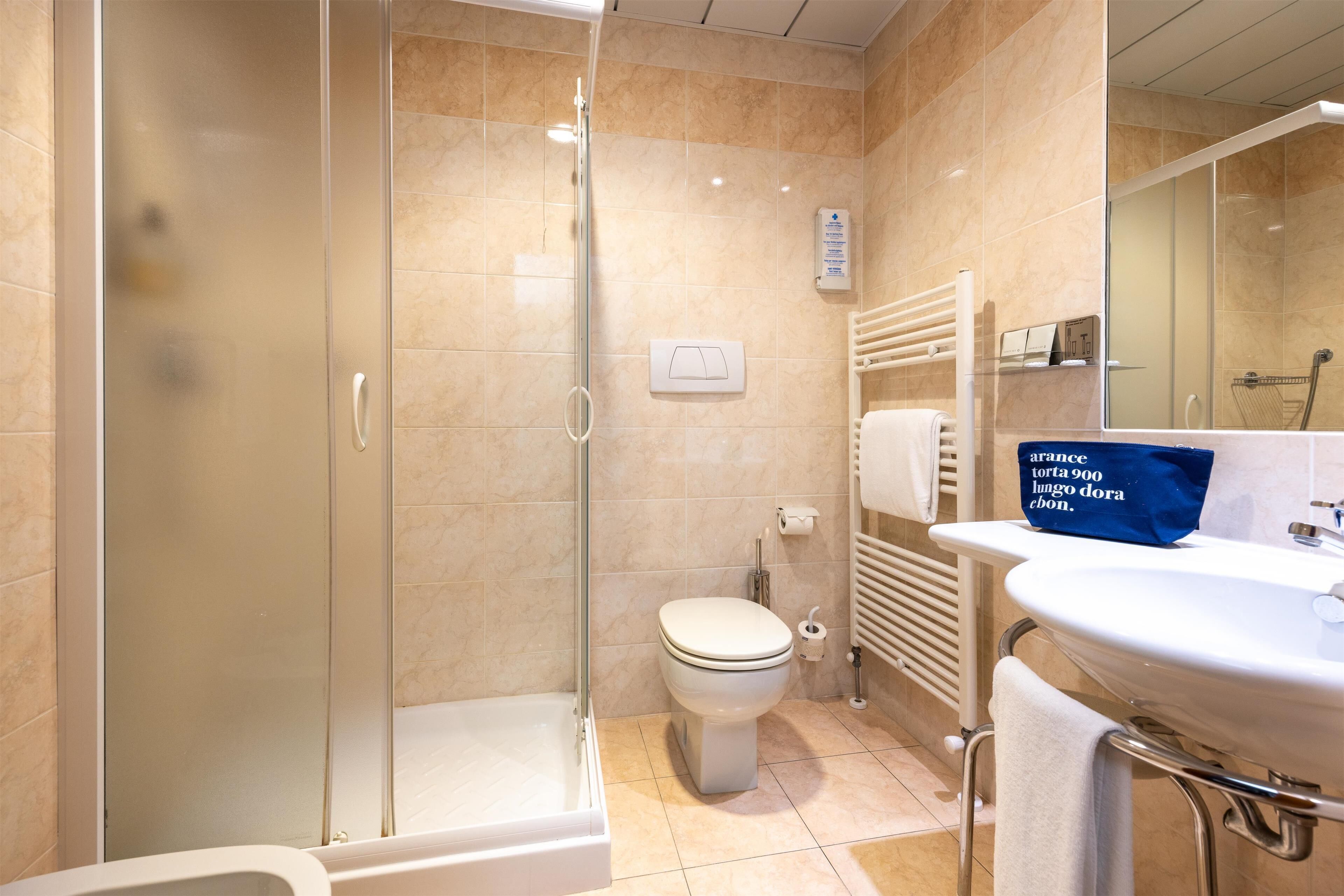 Un bagno con cabina doccia in vetro, un water, un lavandino con un asciugamano e uno specchio.