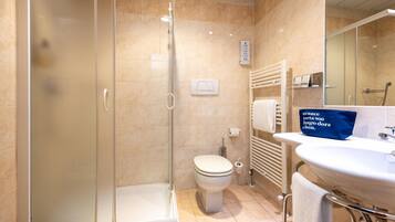 Un bagno con cabina doccia in vetro, un water, un lavandino con un asciugamano e uno specchio.