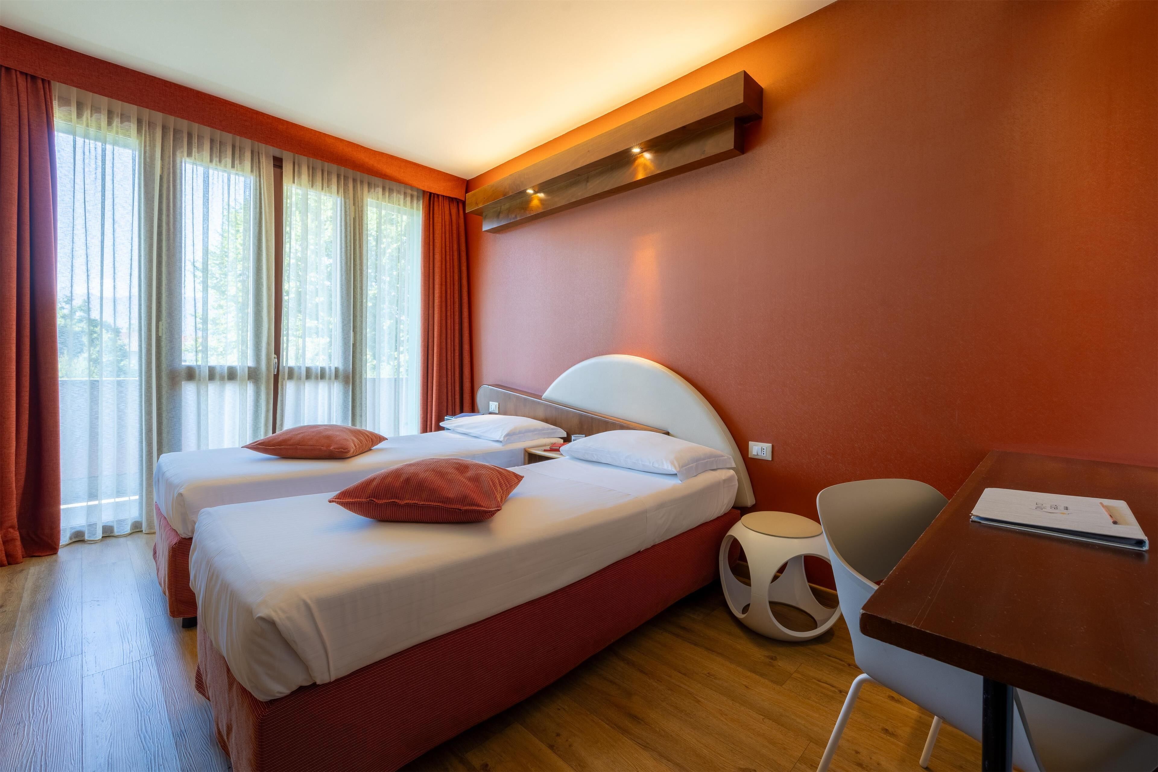 A hotel room with two beds, a desk, and a chair.