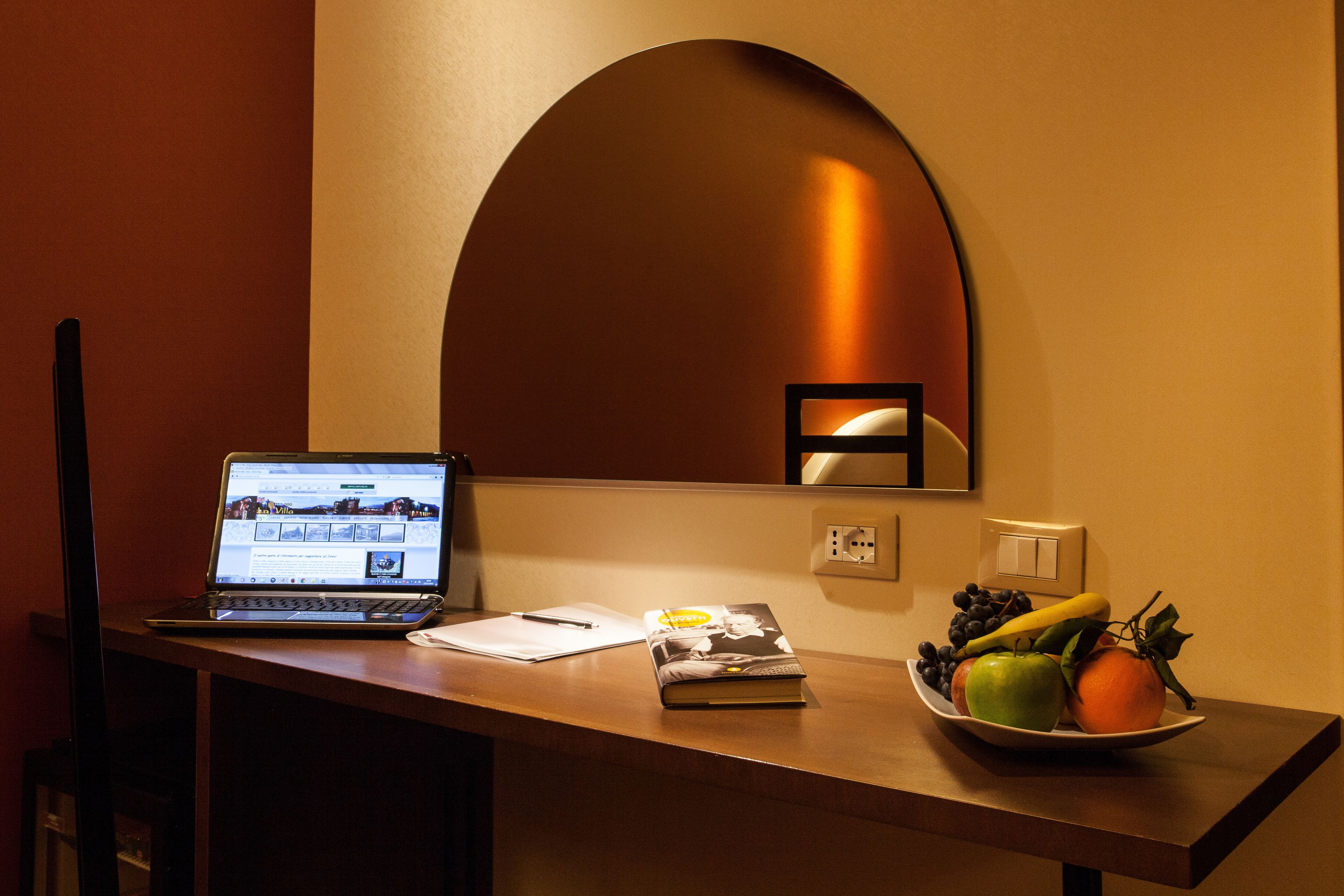 A desk with a laptop, a notebook, a book, and a bowl of fruit.