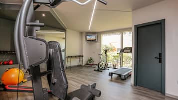 Un gimnasio moderno con equipo de ejercicio, una cinta de correr y una mesa pequeña con mancuernas.