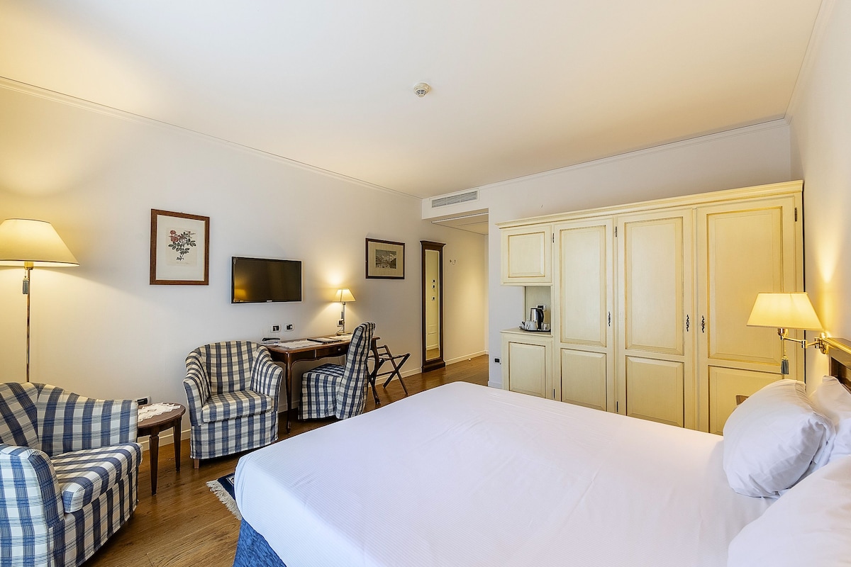 A hotel room with a large bed, two armchairs, a desk, a television, and a wardrobe.