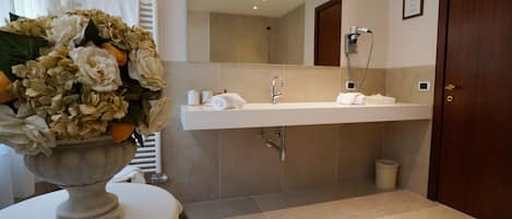 A modern bathroom with a large mirror, a sink, and a shower. There is a vase with flowers on a table in the foreground.