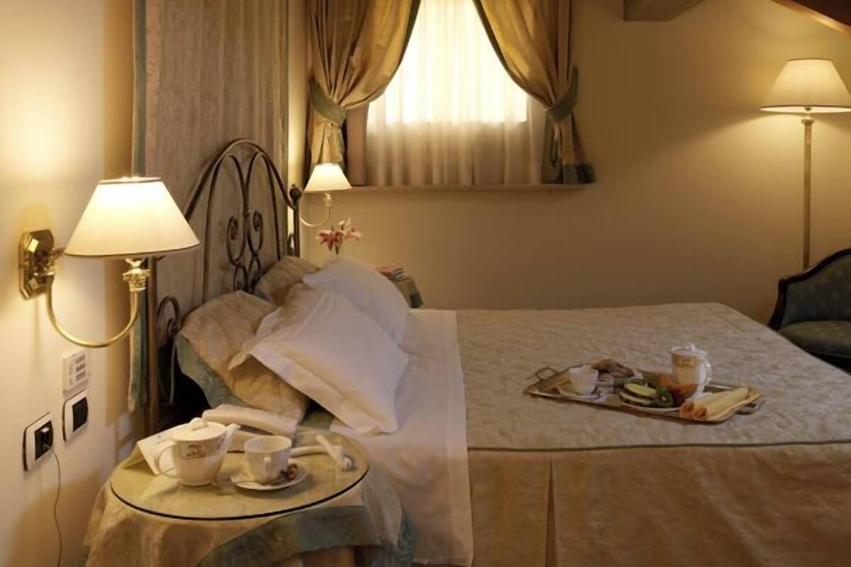 A hotel room with a bed, bedside lamps, a table with a tray of breakfast items, and a window with curtains.