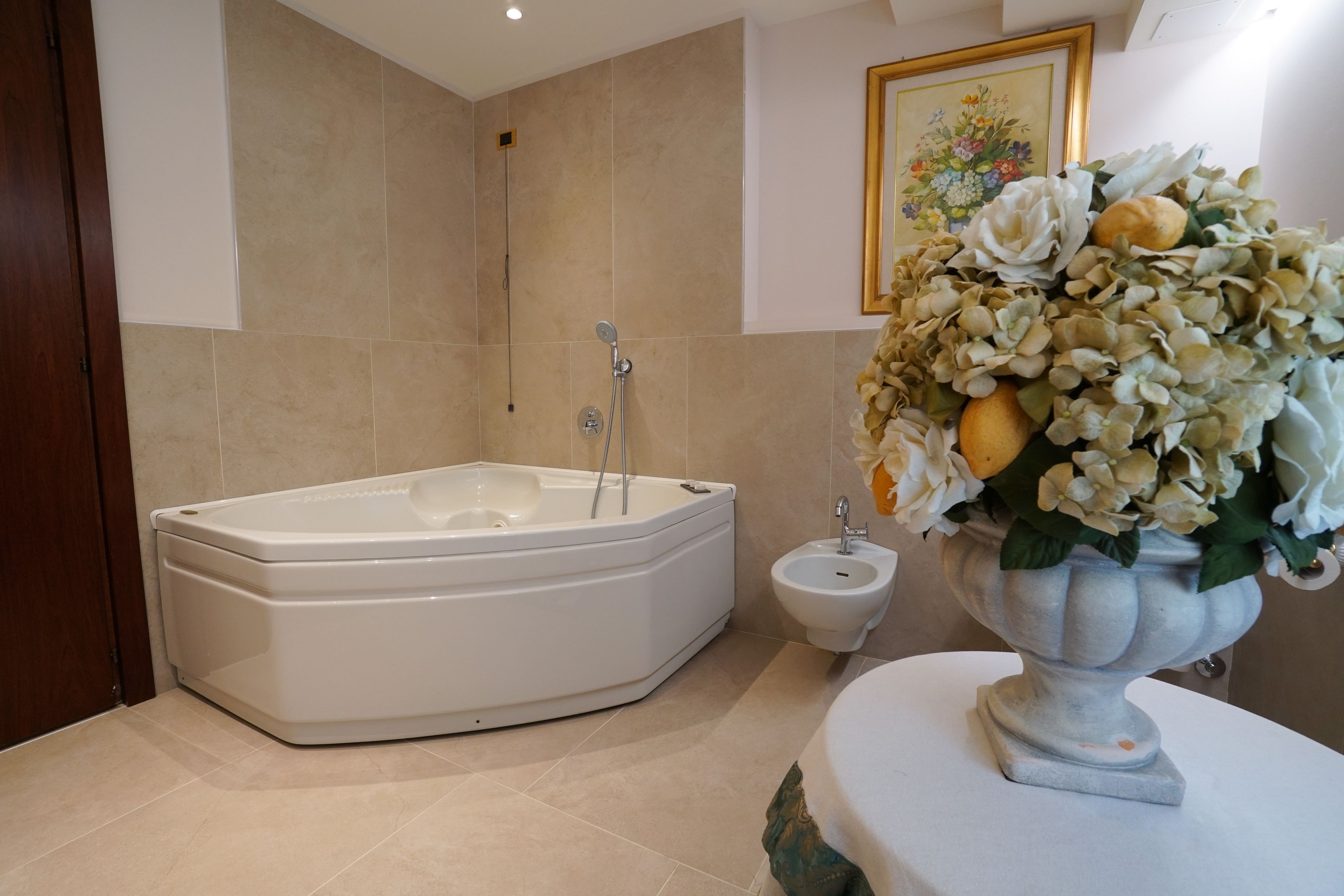 A bathroom with a bathtub, a bidet, and a vase with flowers on the counter.