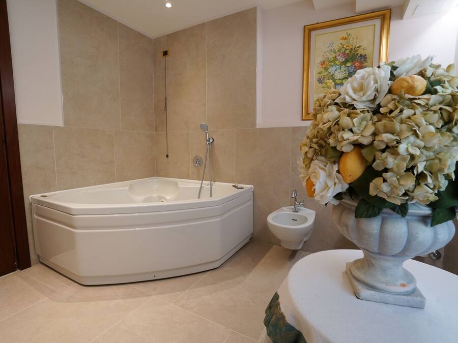 A bathroom with a bathtub, a bidet, and a vase with flowers on the counter.