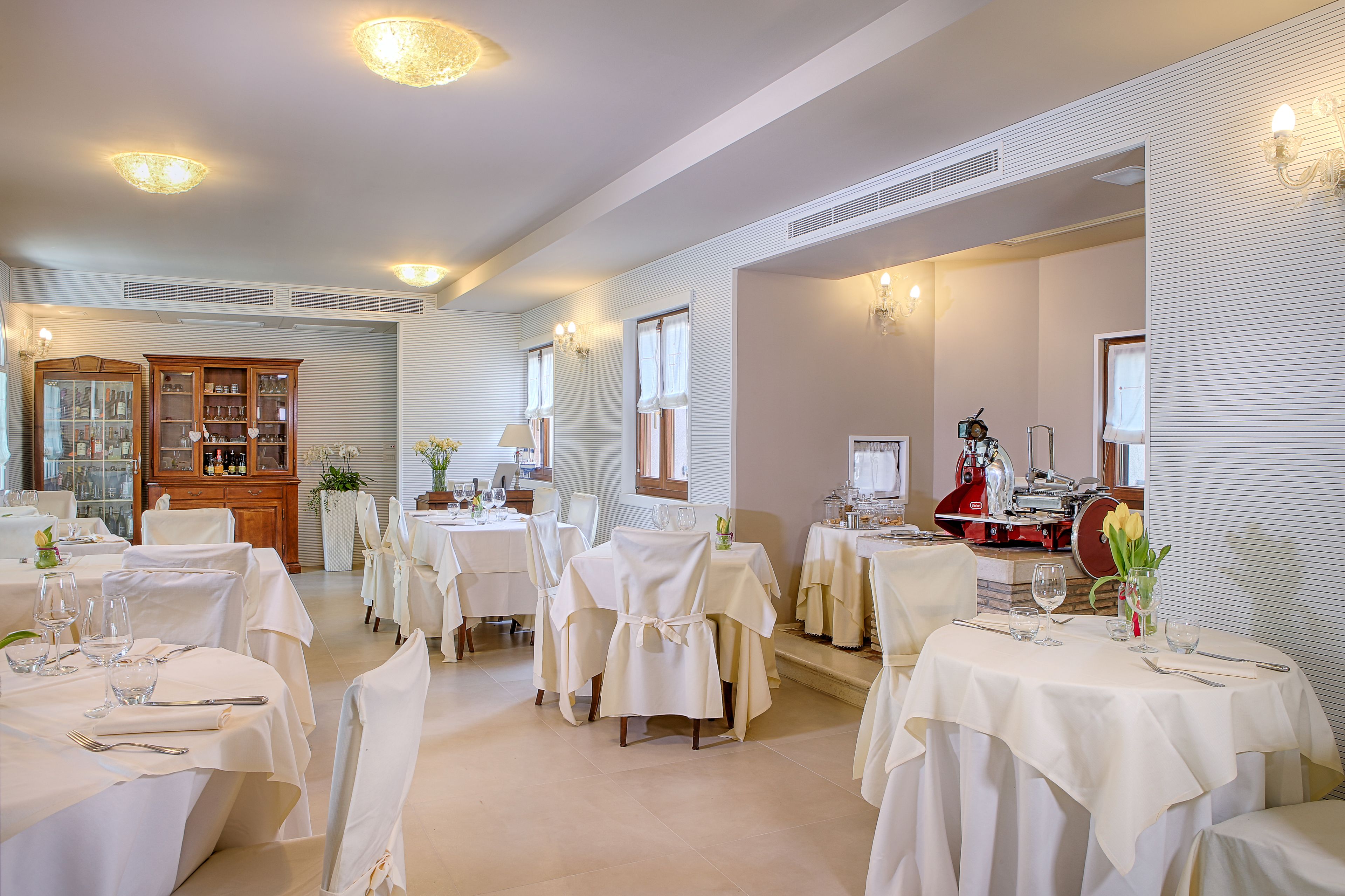 A dining area with multiple tables set for service, a wooden cabinet, and a red machine in the background.