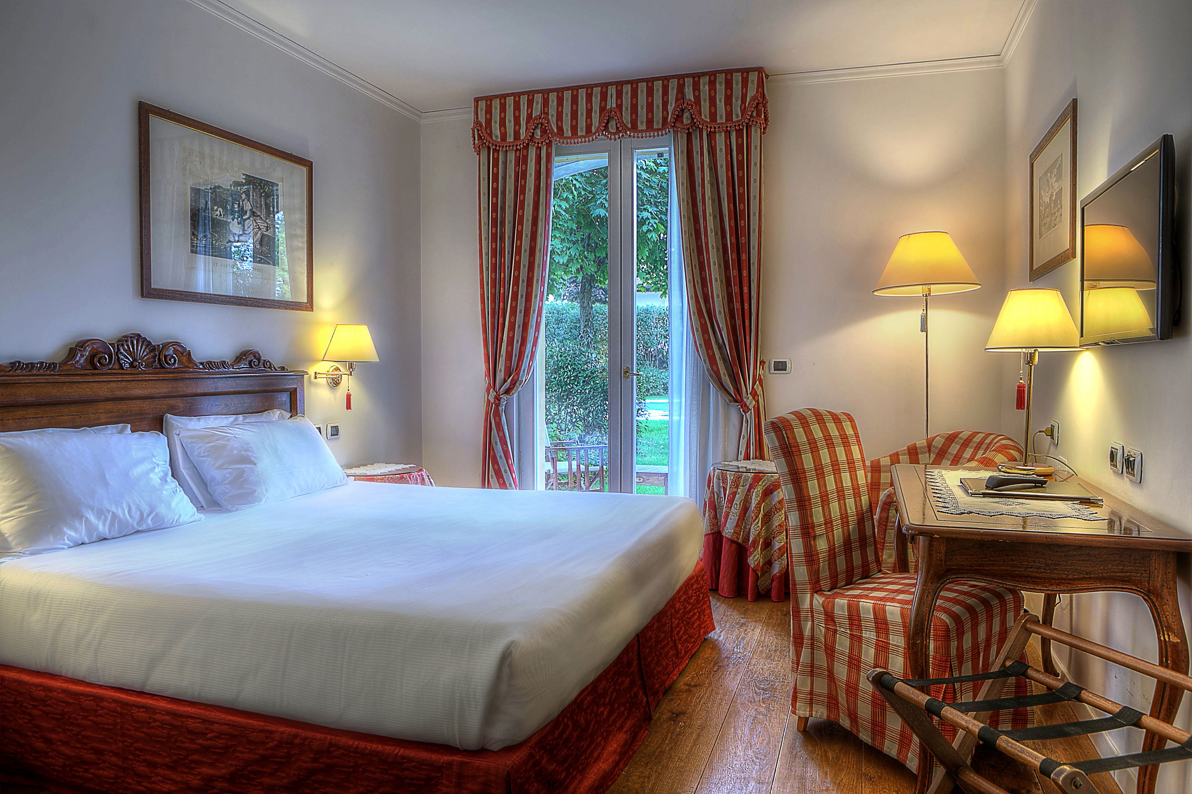 Une chambre d’hôtel avec un grand lit, un bureau avec une chaise, deux lampes et une fenêtre avec des rideaux.