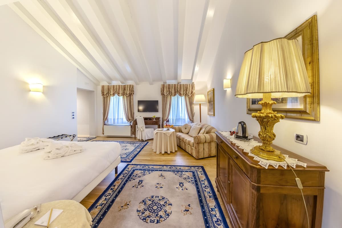 A hotel room with a bed, a sofa, a small table, a lamp, and a TV.