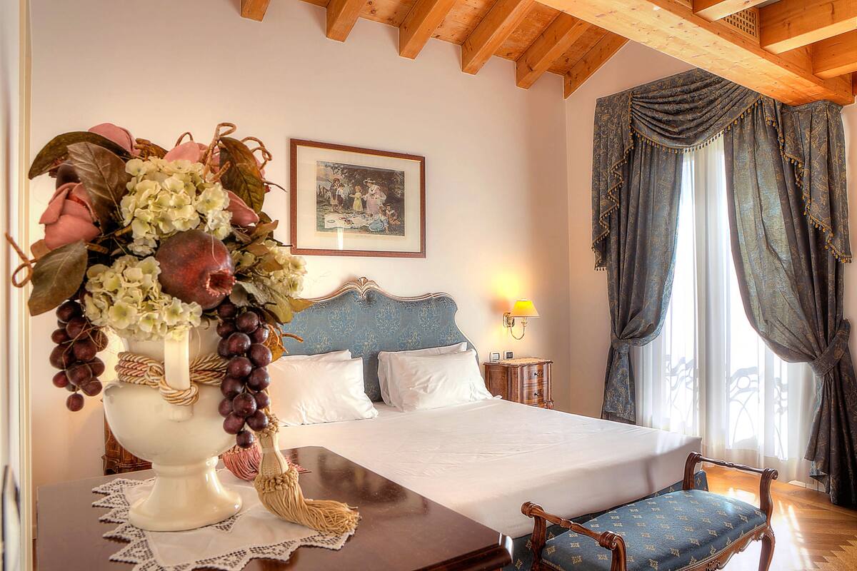A bedroom with a bed, a bedside table, a lamp, a chair, and a decorative vase with flowers.