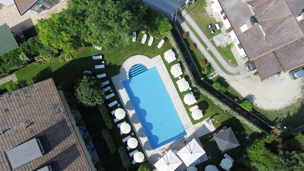 An aerial view of a residential area with a swimming pool surrounded by lounge chairs and umbrellas, adjacent to a road with parked cars.