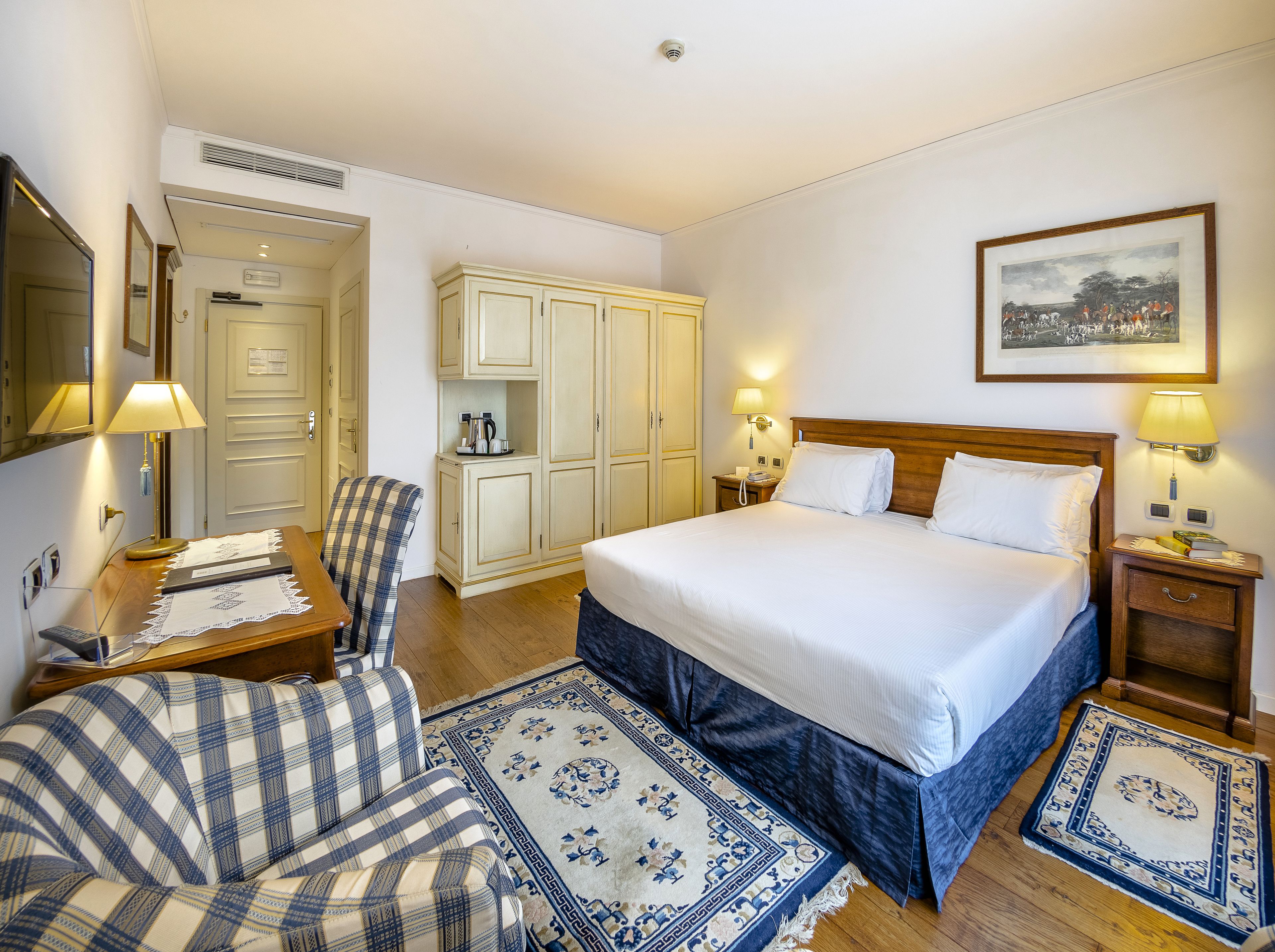 Una camera d'albergo con un letto grande, una sedia, una scrivania, un armadio e un quadro appeso al muro.