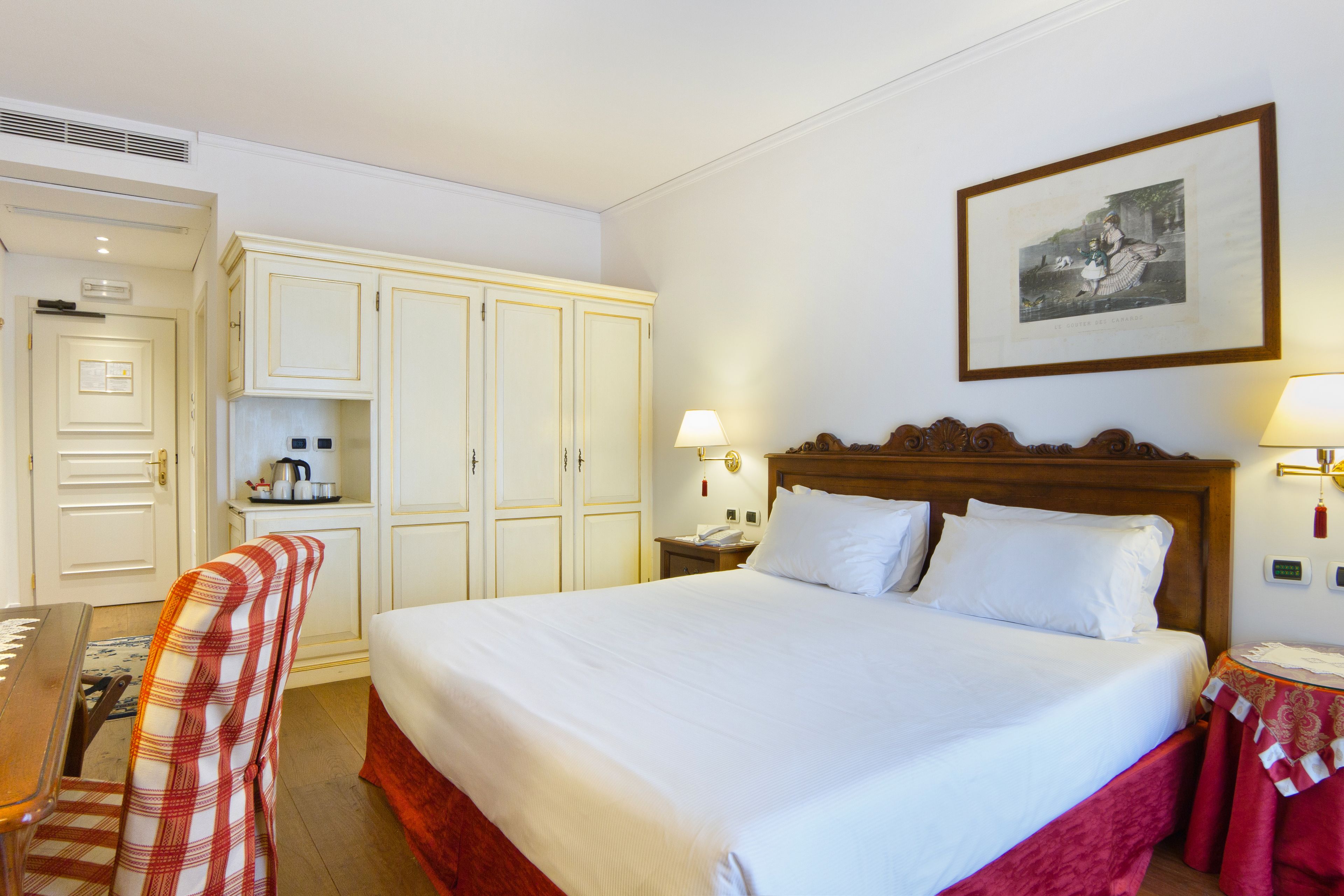 Une chambre d’hôtel avec un grand lit, un bureau et une chaise. Il y a un tableau encadré au mur et une lampe sur la table de chevet.