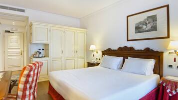 Une chambre d’hôtel avec un grand lit, un bureau et une chaise. Il y a un tableau encadré au mur et une lampe sur la table de chevet.