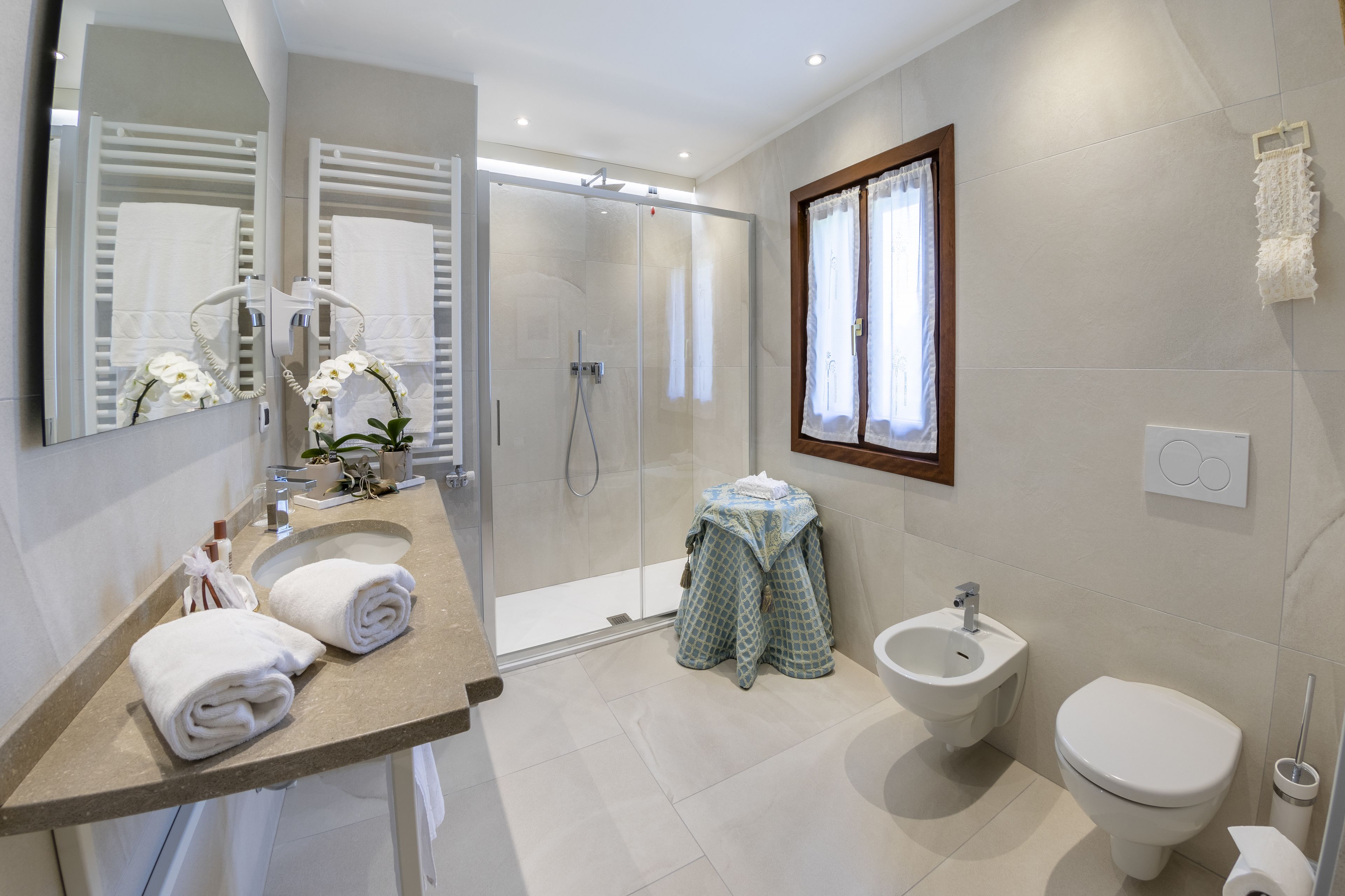 A modern bathroom with a glass-enclosed shower, a bidet, a toilet, and a vanity with towels.