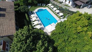 Vista aerea di una piscina residenziale con lettini e ombrelloni, circondata da alberi e una casa.