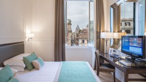 A hotel room with a bed, a desk with a computer, and a large window offering a view of buildings. - Internazionale Domus (Rome)