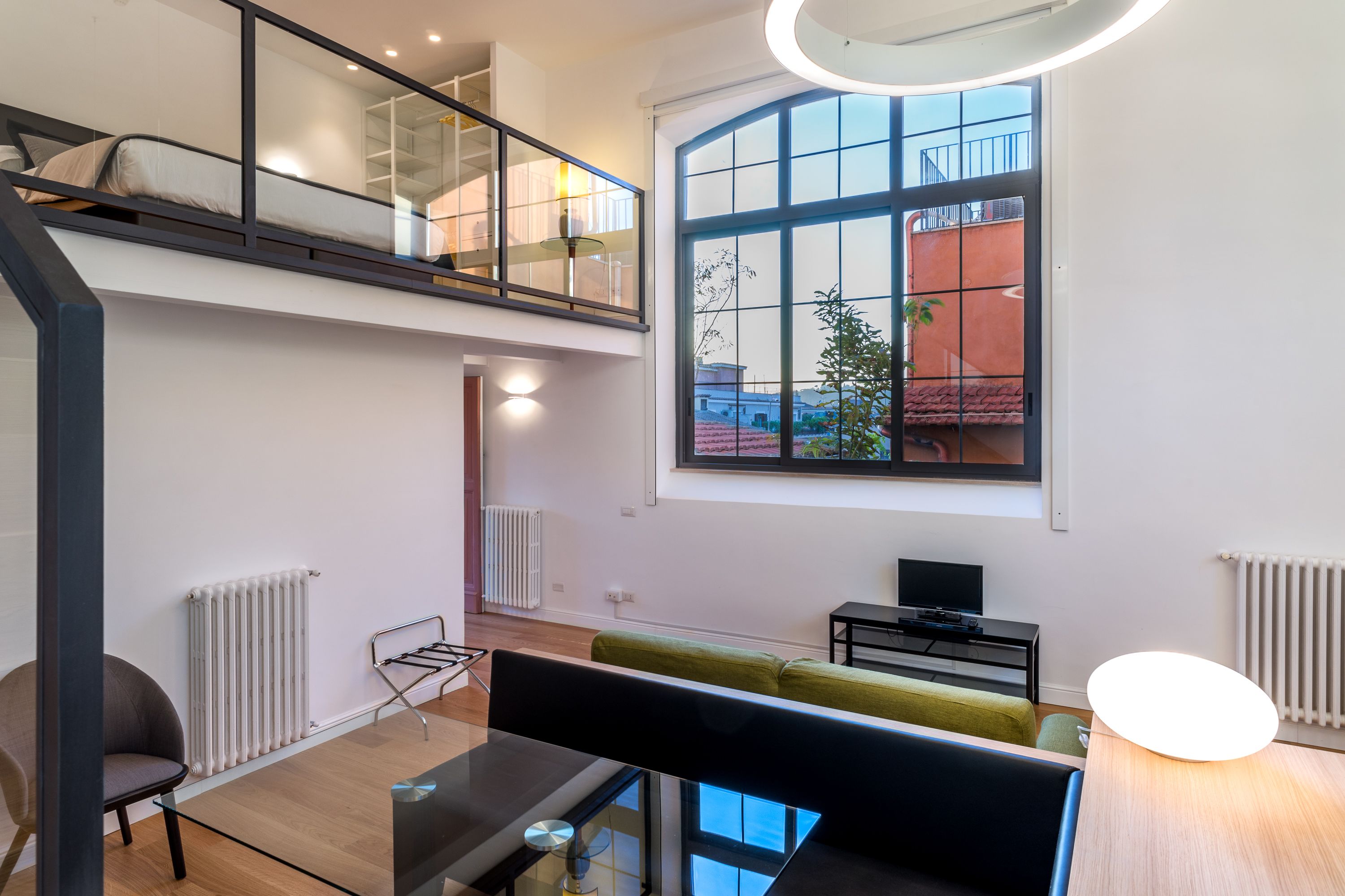 A modern apartment with a loft bedroom, a dining area, and a large window offering a view of the city.