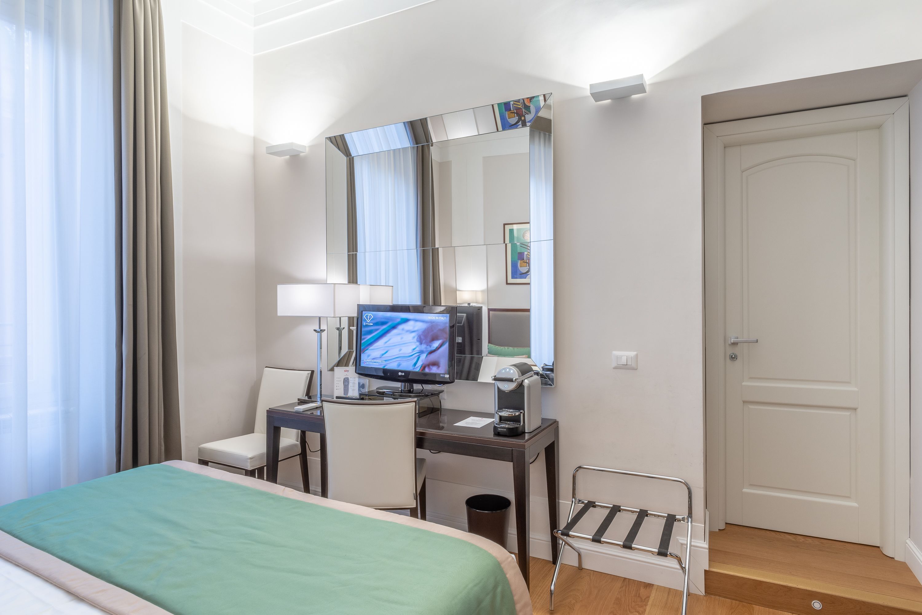 A hotel room with a bed, desk, chair, TV, and a door.