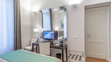 A hotel room with a bed, desk, chair, TV, and a door.