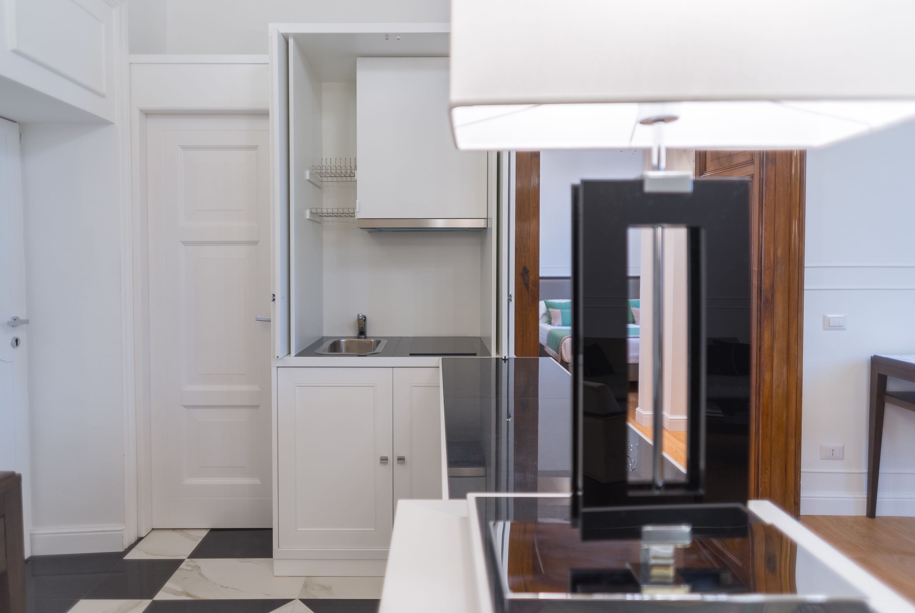 A modern kitchen with white cabinetry, a black and white checkered floor, and a built-in oven.