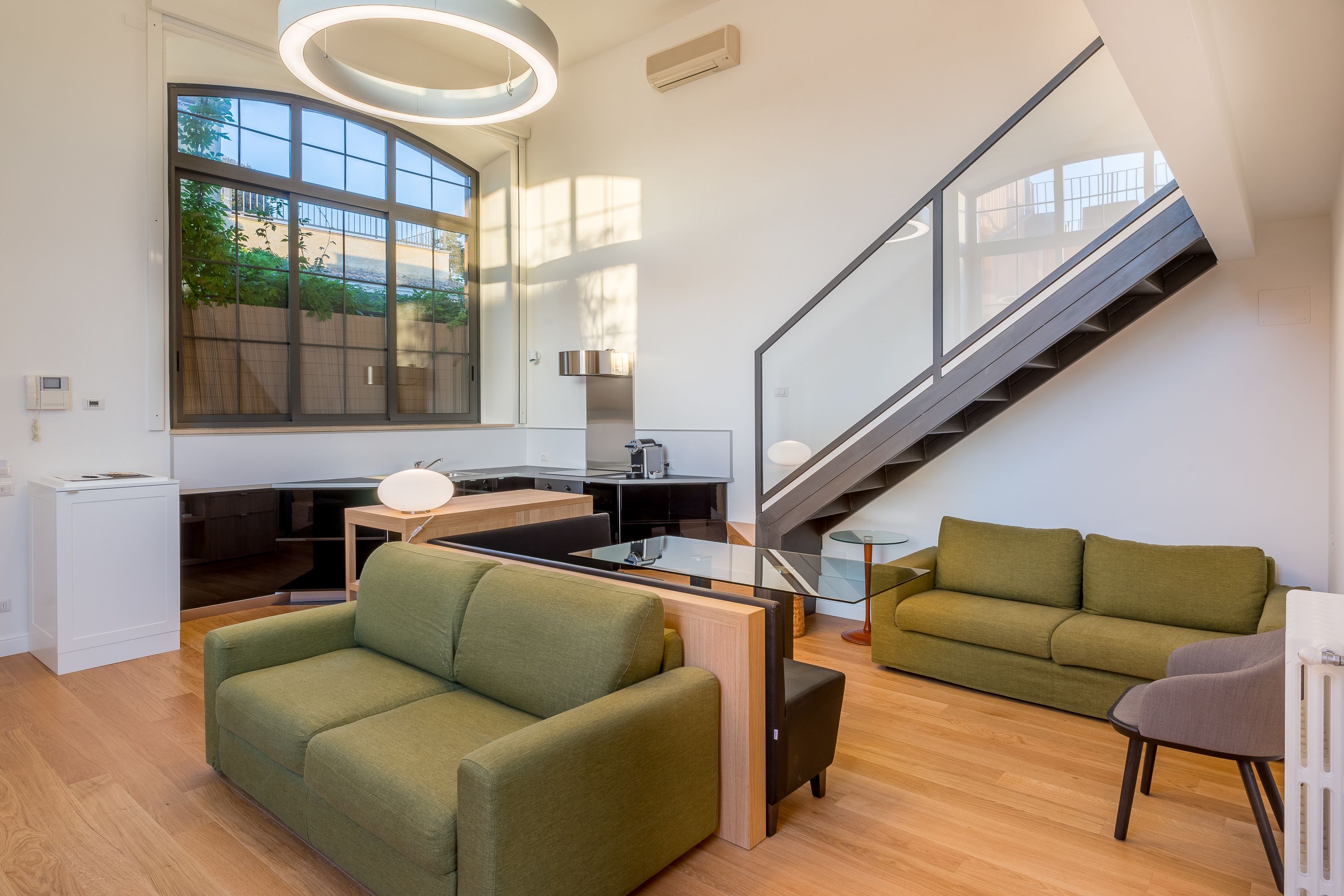 Een moderne woonkamer met een groene bank, een glazen salontafel en een trap.