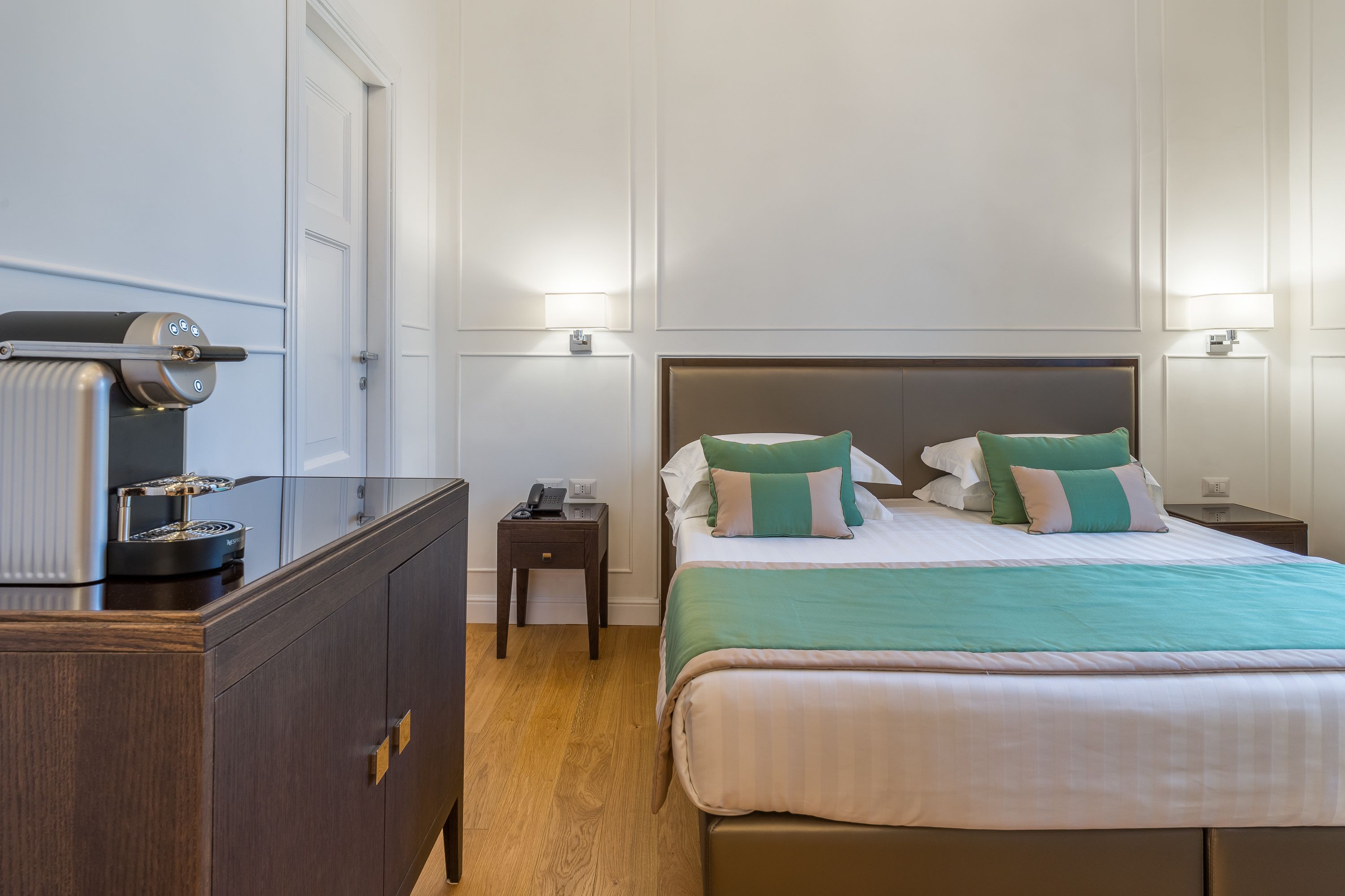 A hotel room with a bed, bedside table, lamp, and a minibar.