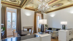 A modern hotel room with a dining area, a sofa set, a chandelier, and a view of the cityscape. - Internazionale Domus (Rome)