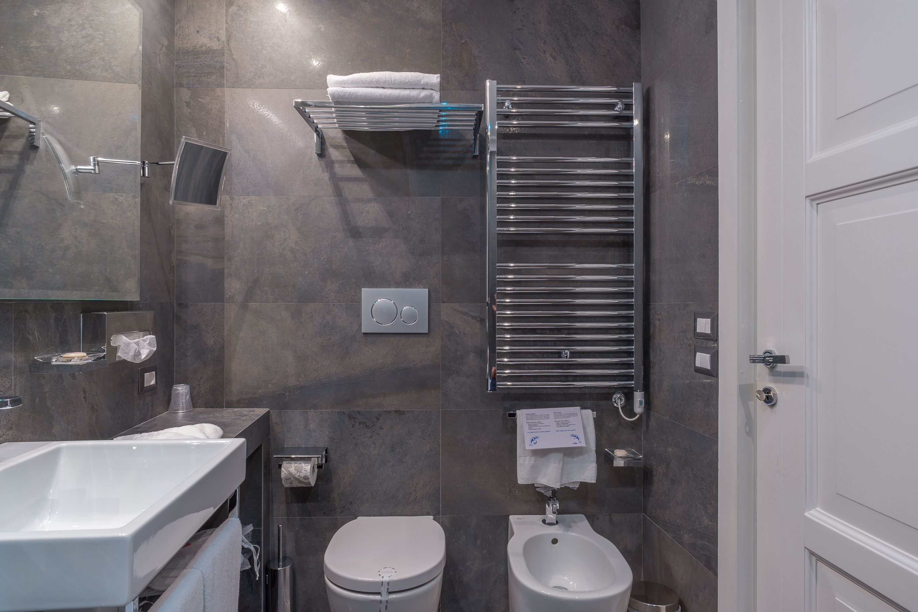 A modern bathroom with a large sink, toilet, bidet, and towel racks.