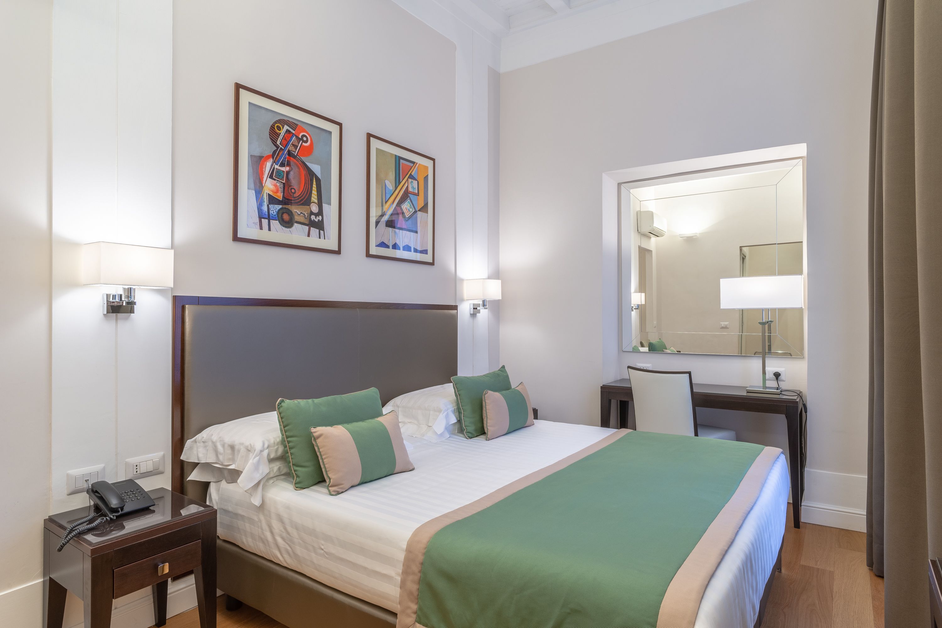 A hotel room with a large bed, bedside tables, a desk, and a mirror.