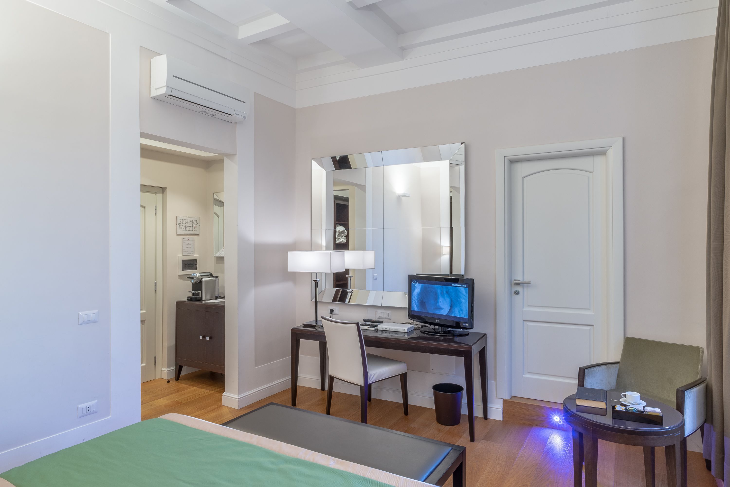 Una habitación de hotel con cama, escritorio, silla, computadora y una pequeña mesa con una taza.