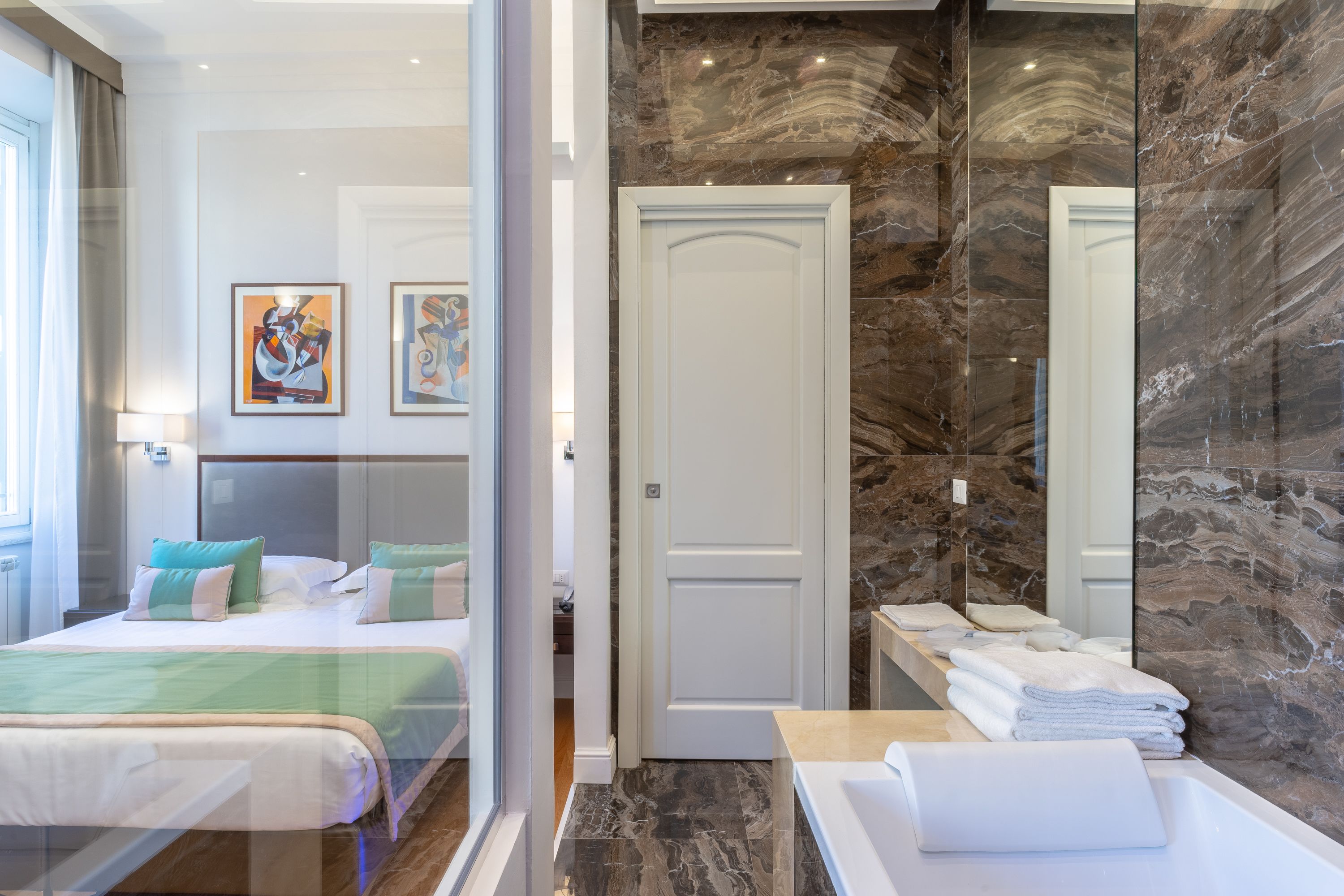 A hotel room with a bed, a bathroom with a marble wall, and a door.