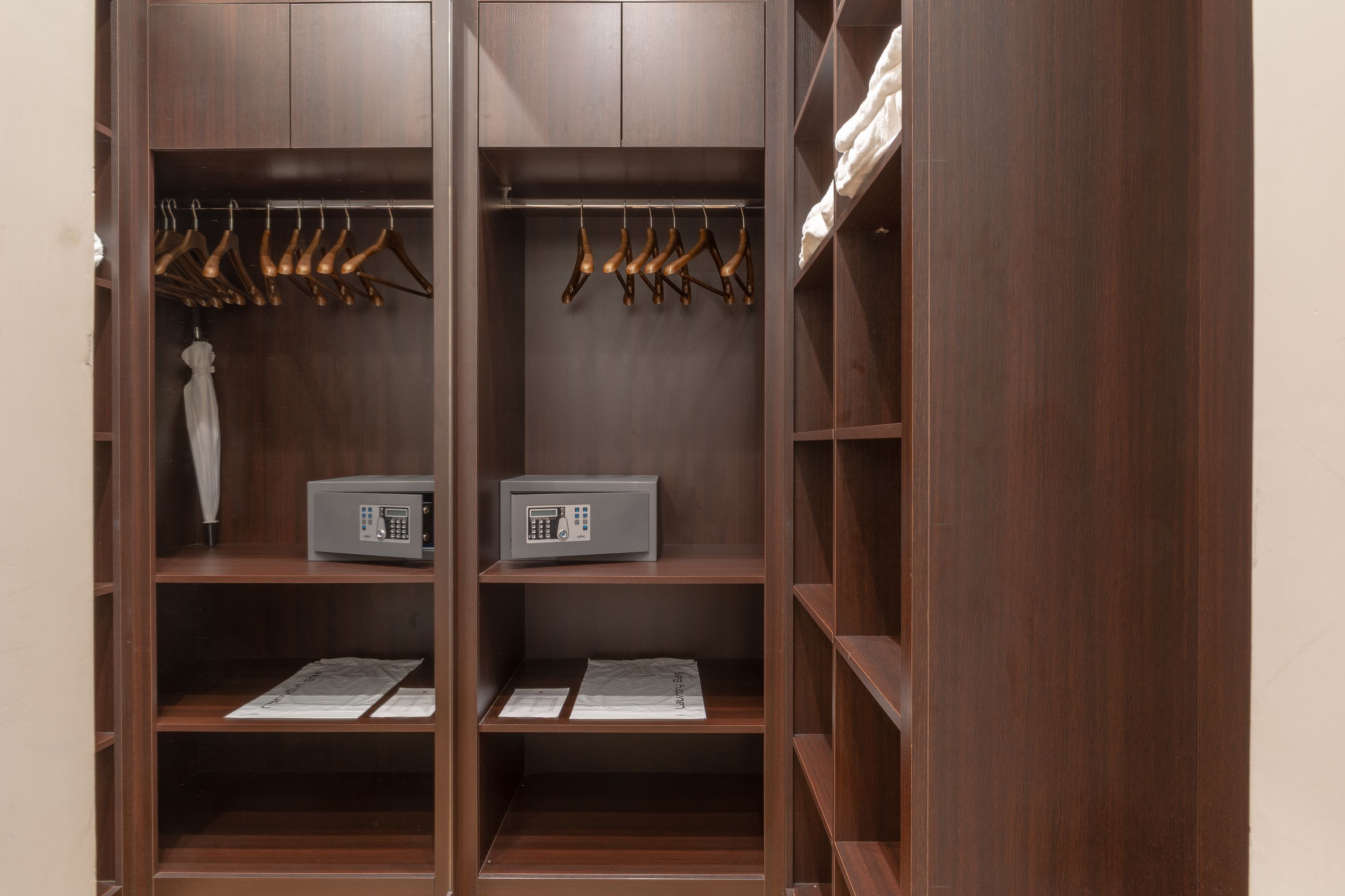 A wooden wardrobe with multiple shelves, a hanging rod, and a microwave on one of the shelves.