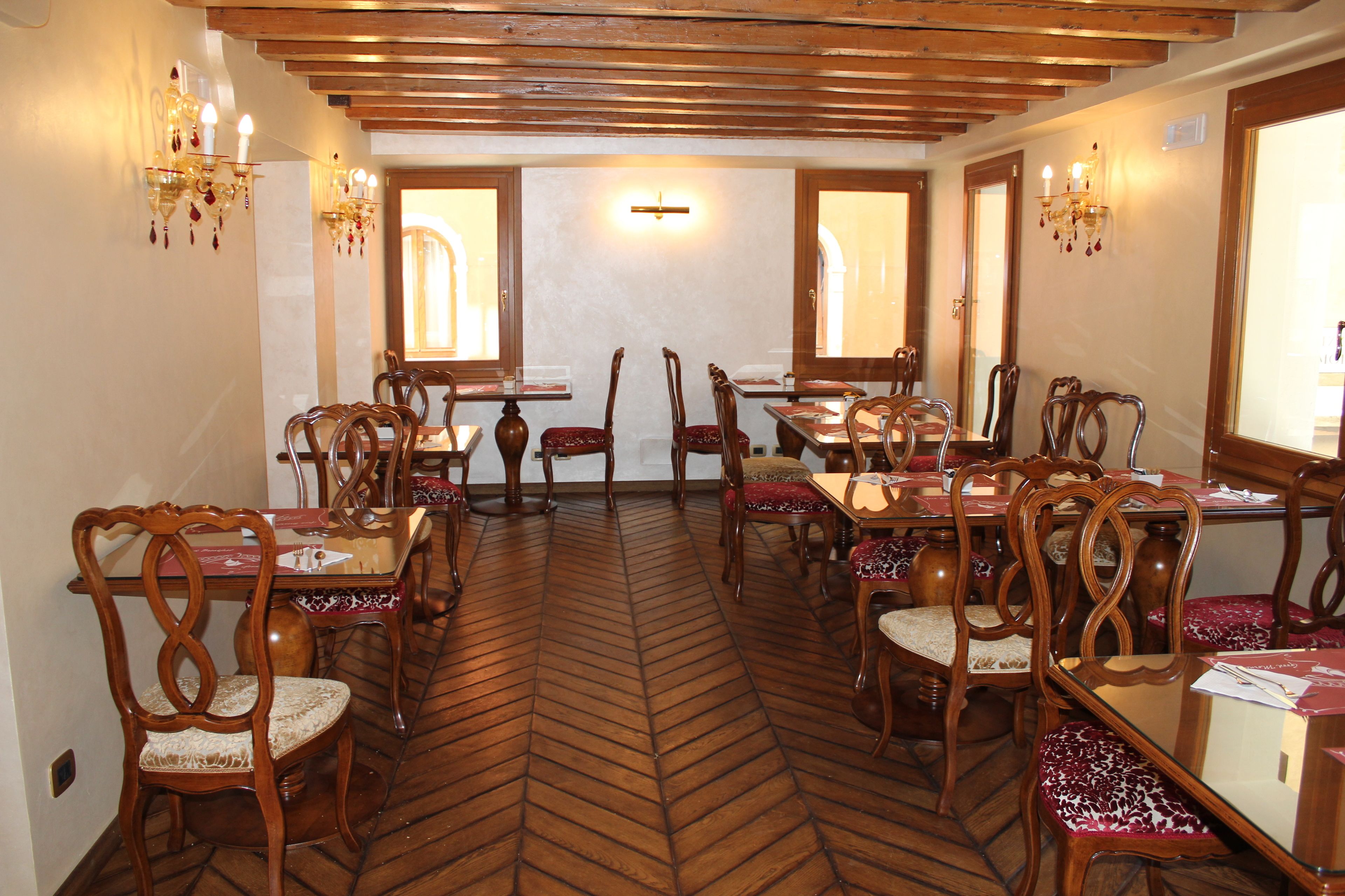 Un espace repas avec des tables et des chaises en bois, un parquet à motifs en chevrons et des lustres fixés au mur.