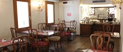 Un restaurante con muebles de madera, un suelo con diseño de espiga y una cocina visible a través de una puerta abierta.