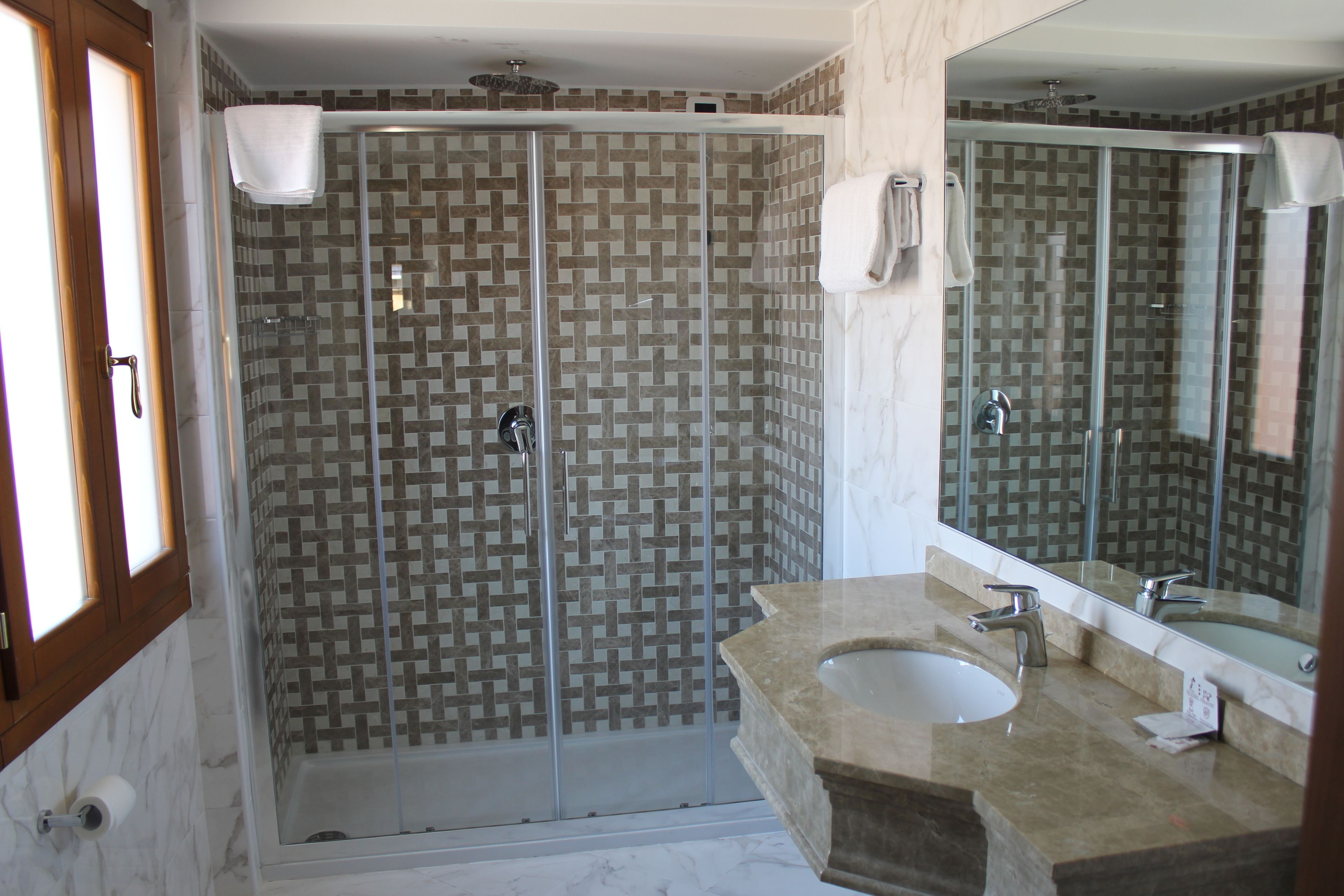 A bathroom with a glass-enclosed shower, a sink, and a mirror.