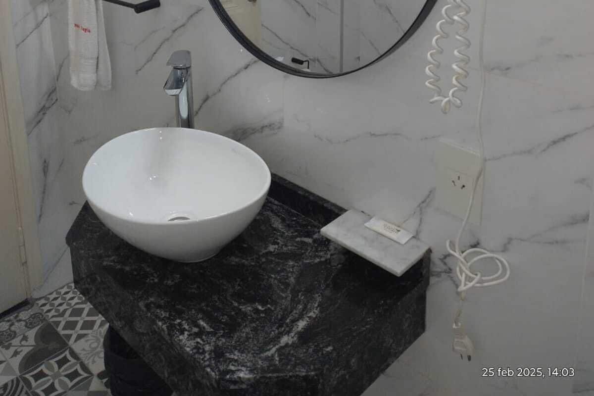 A bathroom with a white marble sink, a round mirror, and a hairdryer mounted on the wall.