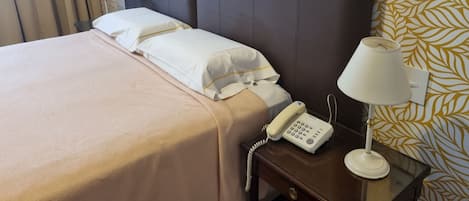 A hotel room with a bed, a bedside lamp, a telephone, and a patterned wall.