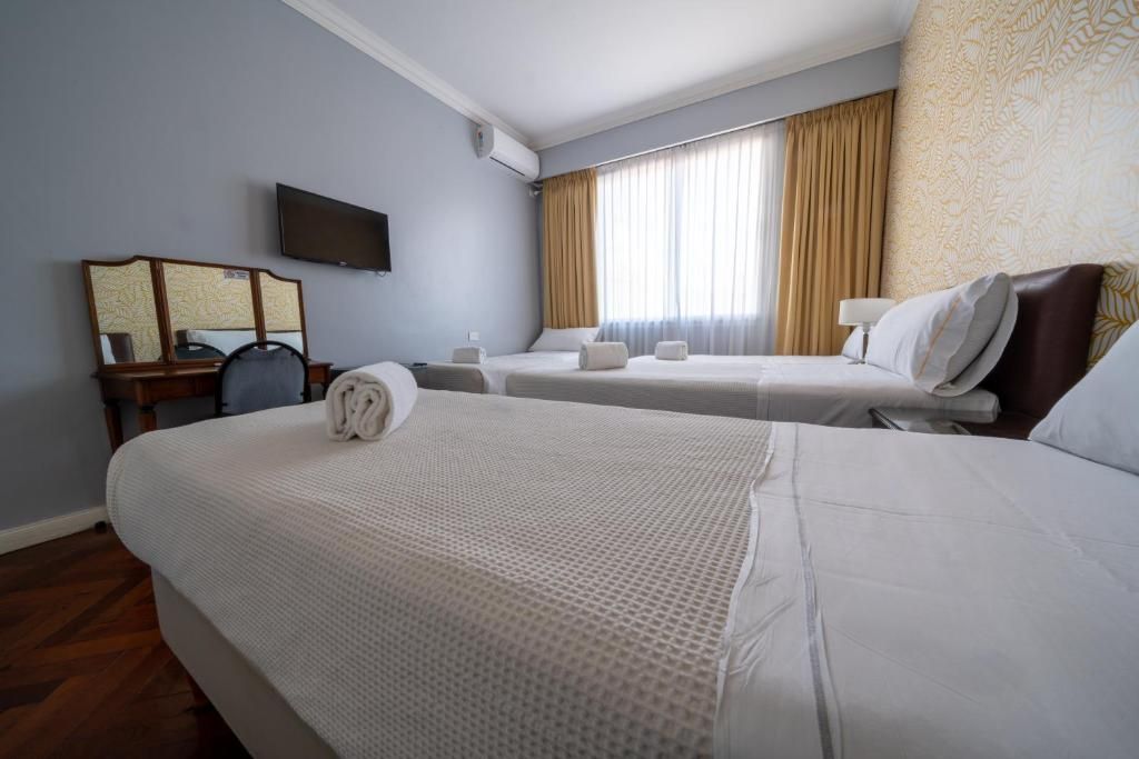 Habitación de hotel con dos camas, un televisor de pantalla plana, un escritorio con silla y un ventanal con cortinas.