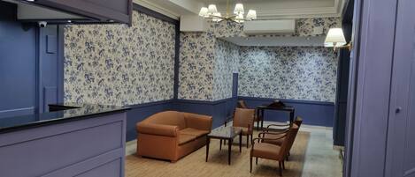 Une pièce avec un papier peint à motifs floraux bleus et blancs, un canapé en cuir marron, une table basse en bois et un lustre.