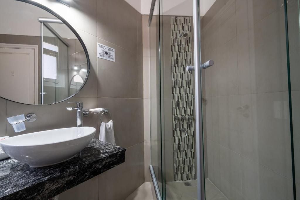 A bathroom with a round mirror, a white sink, and a glass-enclosed shower.