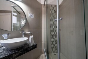 A bathroom with a round mirror, a white sink, and a glass-enclosed shower. - Regis Orho Hotel (Buenos Aires)