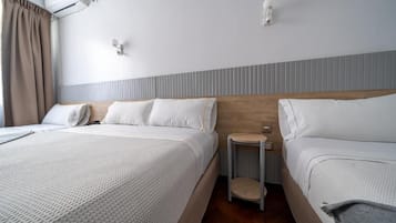 Habitación de hotel con dos camas, una mesita de noche pequeña, aire acondicionado de pared y una ventana con cortinas.