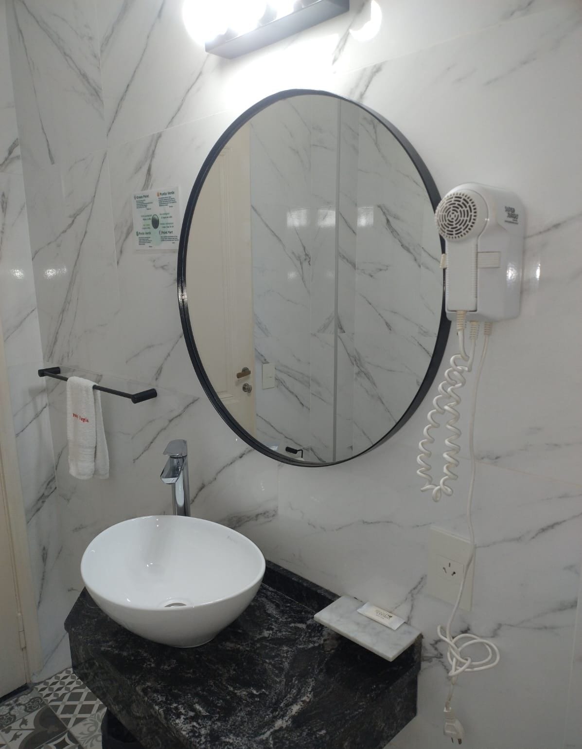 A bathroom with a white marble sink, a round mirror, and a hairdryer mounted on the wall.