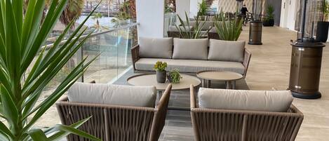 A modern lounge area with a sofa and chairs, a coffee table, and potted plants.