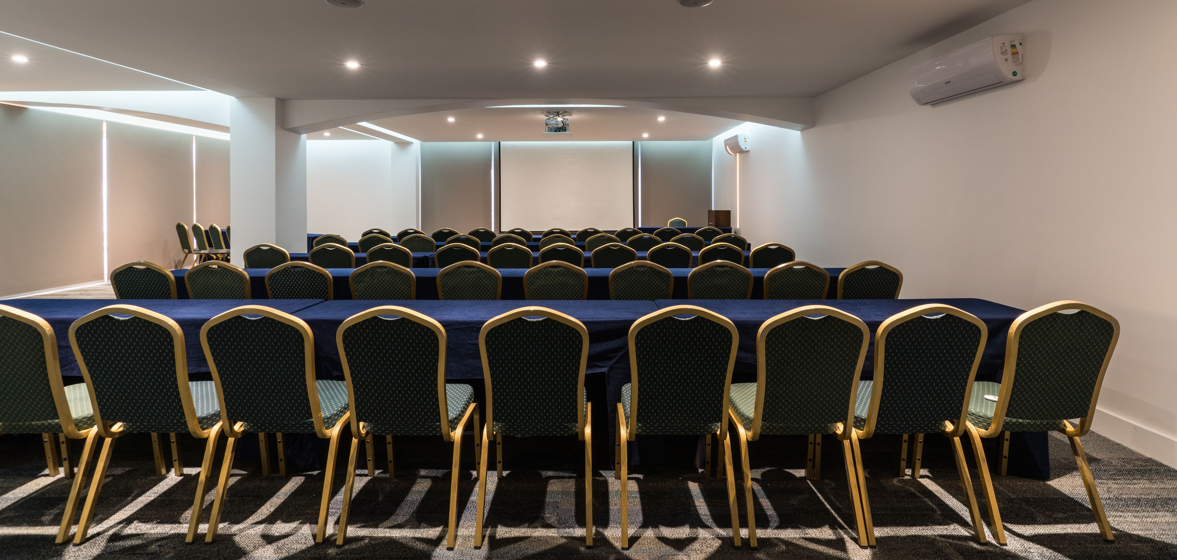 Un salón de conferencias con una larga mesa y sillas, equipado con luces de techo y un equipo de aire acondicionado.