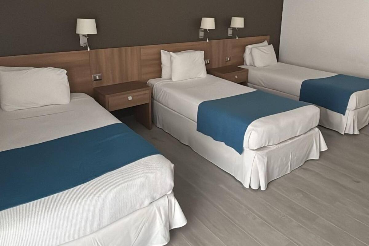 A hotel room with three beds, wooden headboards, and bedside lamps.